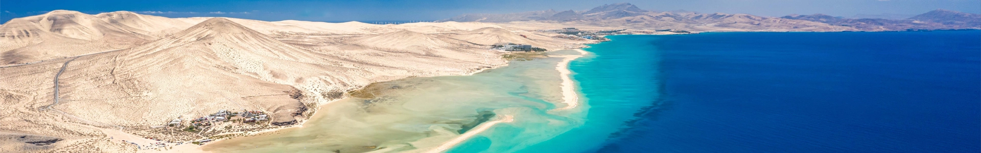 Vue aérienne spectaculaire des plages de sable blanc et des eaux turquoise de Fuerteventura, avec des montagnes désertiques en arrière-plan