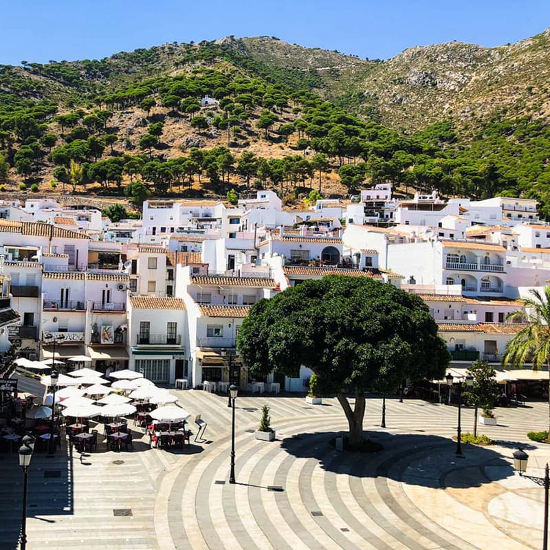 Place centrale de Mijas avec terrasses ombragées, maisons blanches et collines verdoyantes à l’horizon