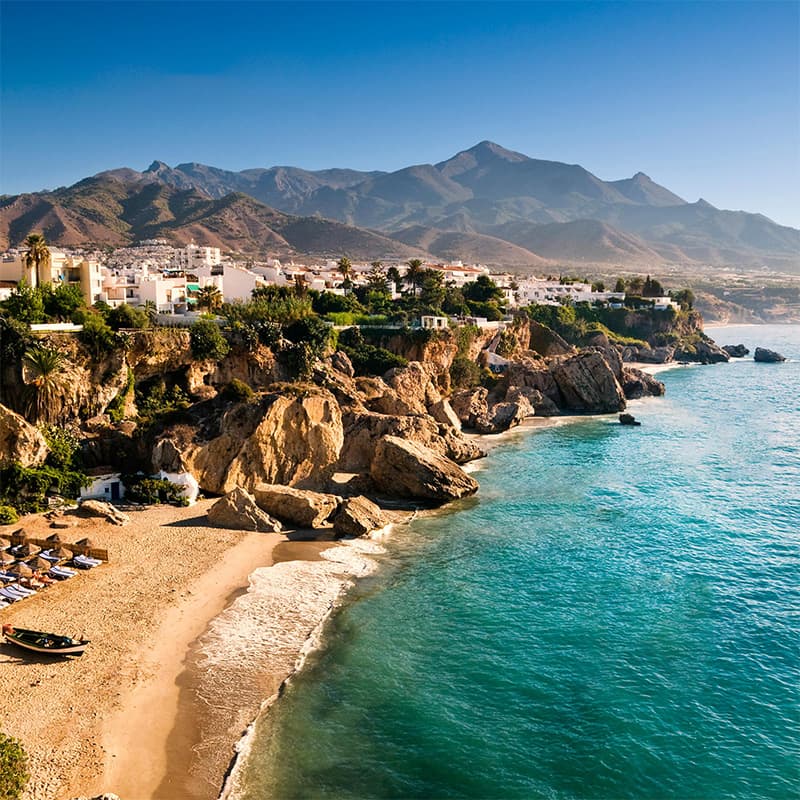 Plage pittoresque de Nerja bordée de falaises, avec des montagnes en arrière-plan et des eaux cristallines