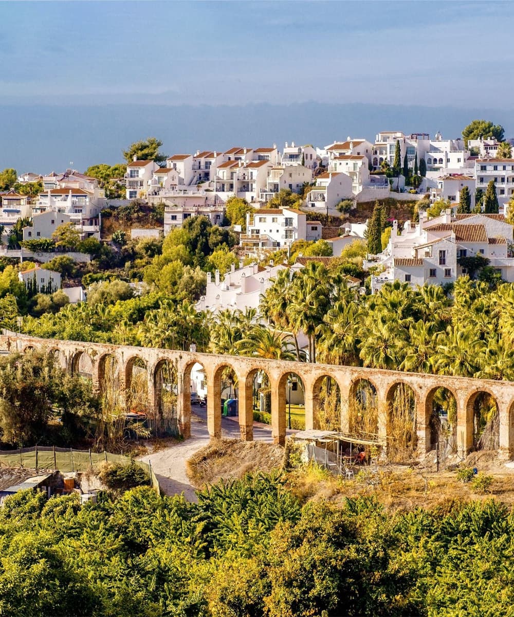 Vue panoramique de Nerja avec ses maisons blanches nichées sur les collines et un aqueduc historique entouré de verdure