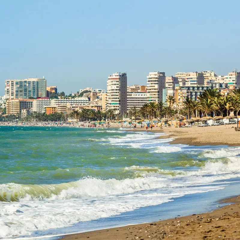 Plage de Torremolinos avec des immeubles en bord de mer et des palmiers sous un ciel ensoleillé