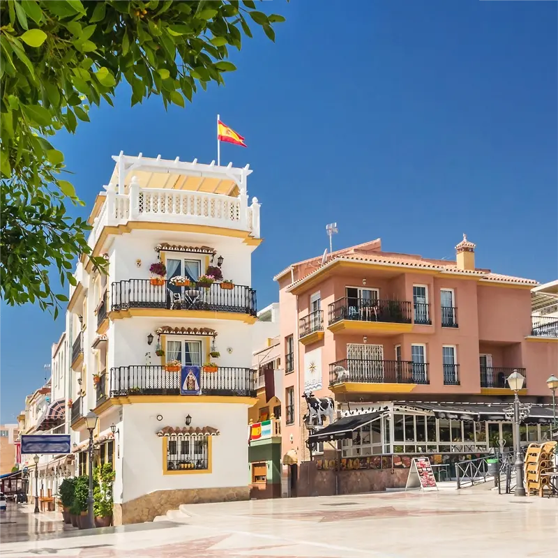 Charmante place du centre-ville de Torremolinos, avec des bâtiments aux balcons fleuris et un drapeau espagnol flottant au sommet